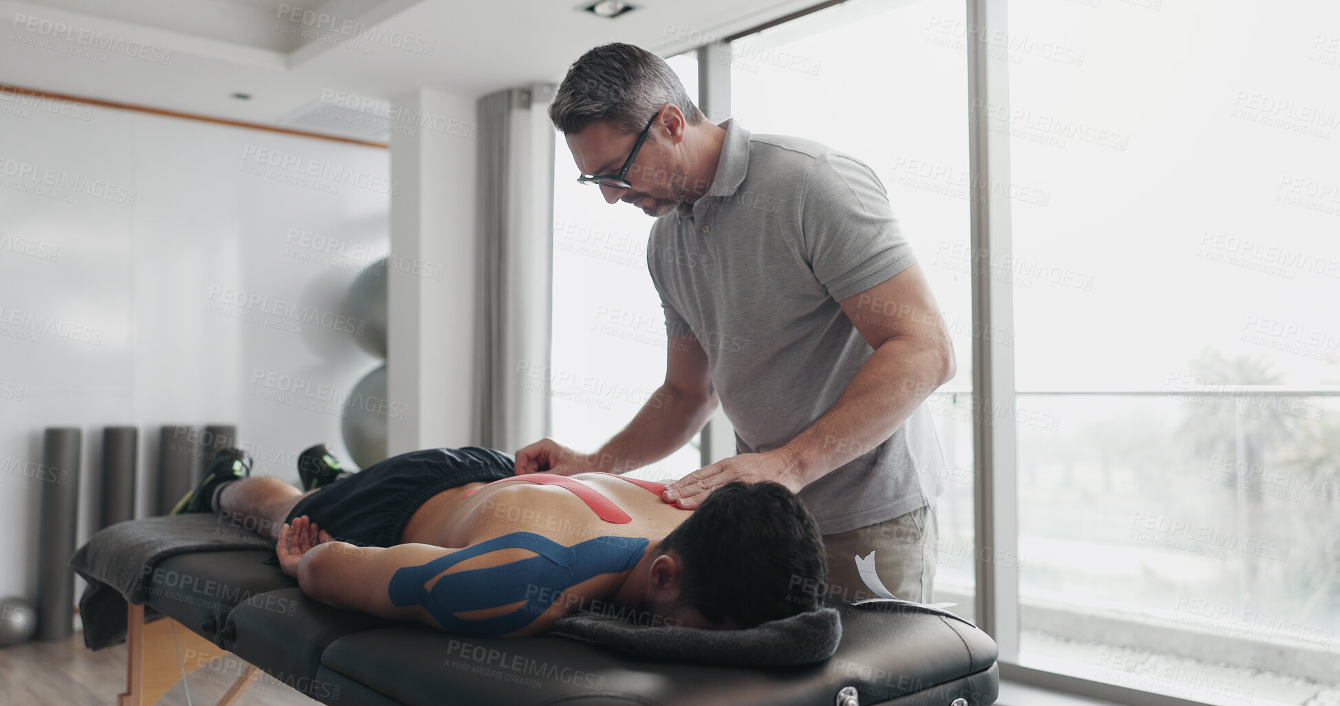 Buy stock photo Physiotherapist, person and tape on bed for recovery process from injury, back pain and help at clinic. People, biokinetics and treatment for rehabilitation with muscle, spine and service at hospital