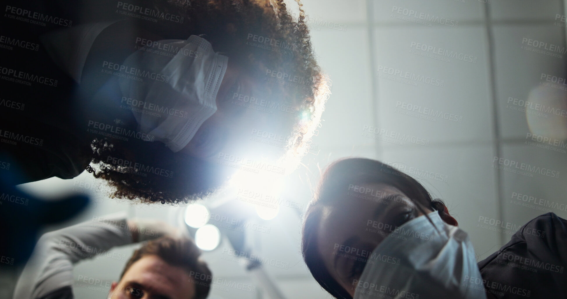 Buy stock photo Dentist, face mask or light below with dental team for hygiene, cleaning or cavity removal at hospital. Lens flare, low angle and medical orthodontist with patient for oral, mouth or gum care exam