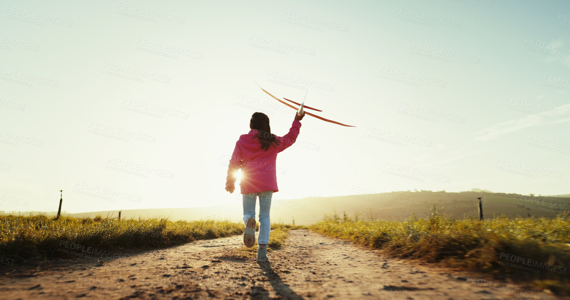 Buy stock photo Child, running outdoor and play with airplane for game, freedom and travel on mockup space. Back, girl and kid with toy plane by sky for flight, vacation and sunset on countryside path for adventure