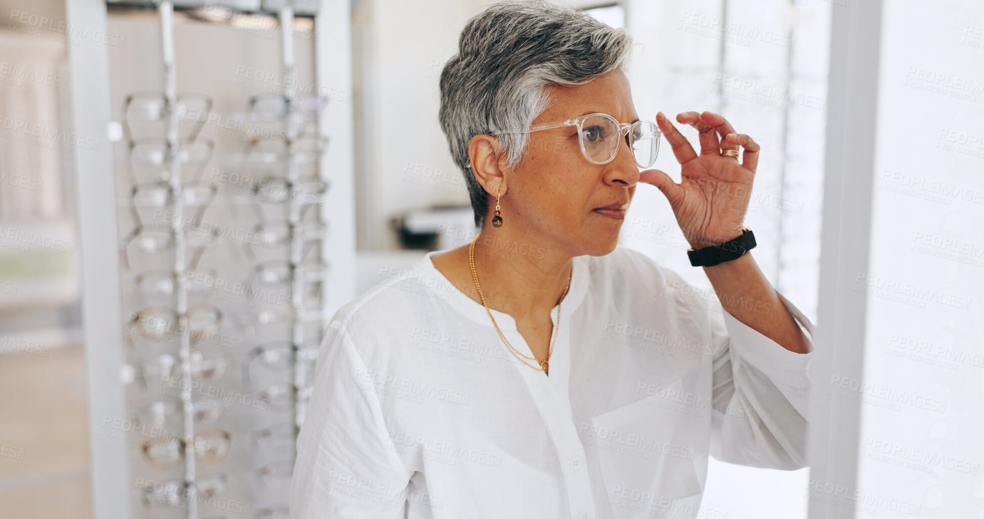 Buy stock photo Mature woman, glasses and check in mirror at clinic for healthy vision, wellness or optometry services. Person, client and customer with decision for prescription eyewear, shopping and frame at store