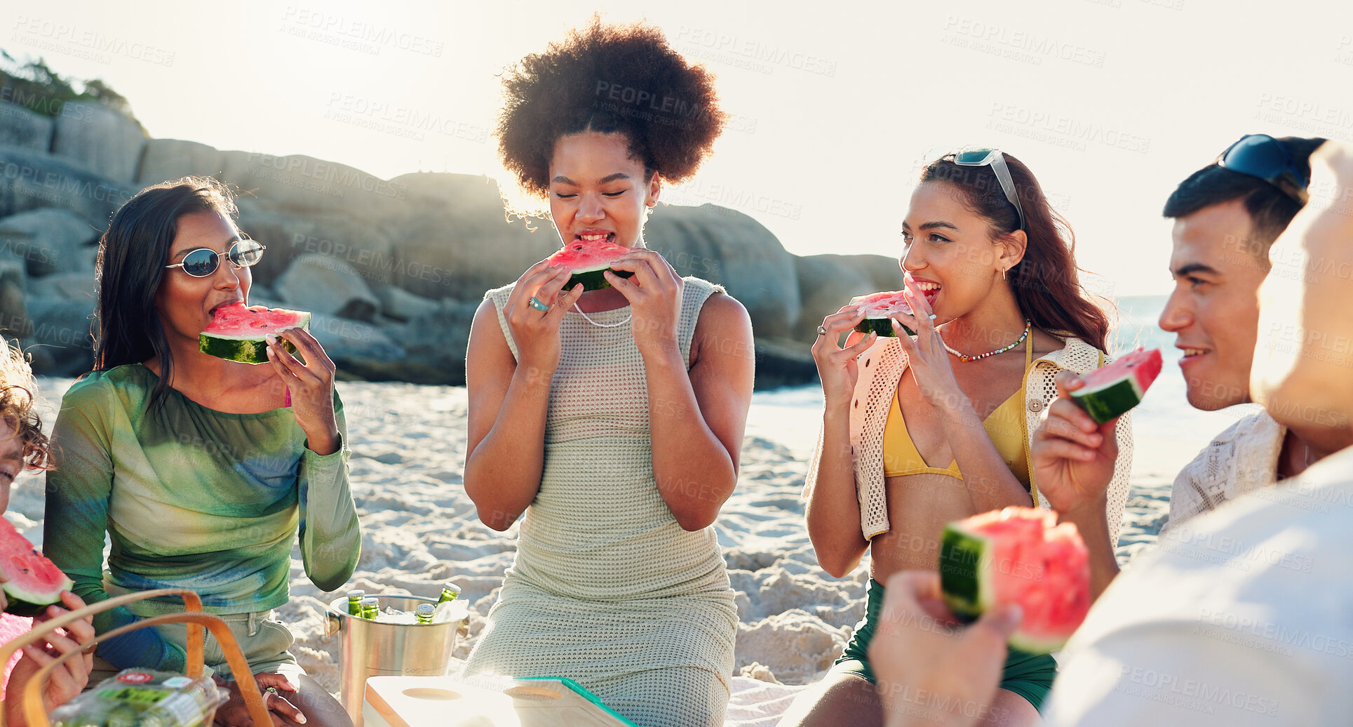 Buy stock photo Group, friends and picnic with watermelon at beach, happy and conversation with reunion on vacation. People, women and men with fruit, sharing and eating together with diversity by ocean at sunset