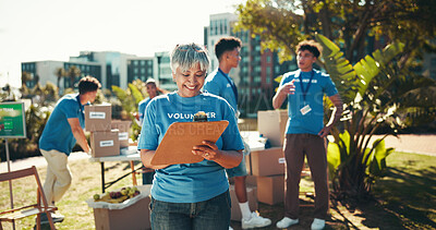 Buy stock photo Happy, volunteers and mature woman with clipboard, charity and inventory for donations, smile and ngo. Outdoor, team and coordinator with checklist for info, community service and boxes for nonprofit