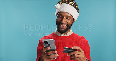 Buy stock photo Christmas, credit card and phone with black man in studio for online shopping, festive discount and holiday sale. Fintech, payment and ecommerce with person on blue background for xmas purchase