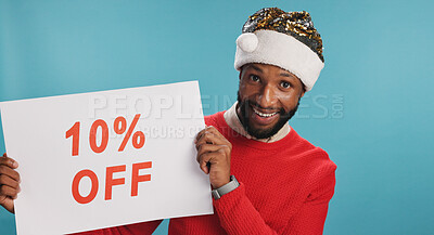 Buy stock photo Board, happy and black man for christmas discount in studio with advertisement for promotion. Excited, poster and African male person with sign for deal with holiday shopping by blue background.