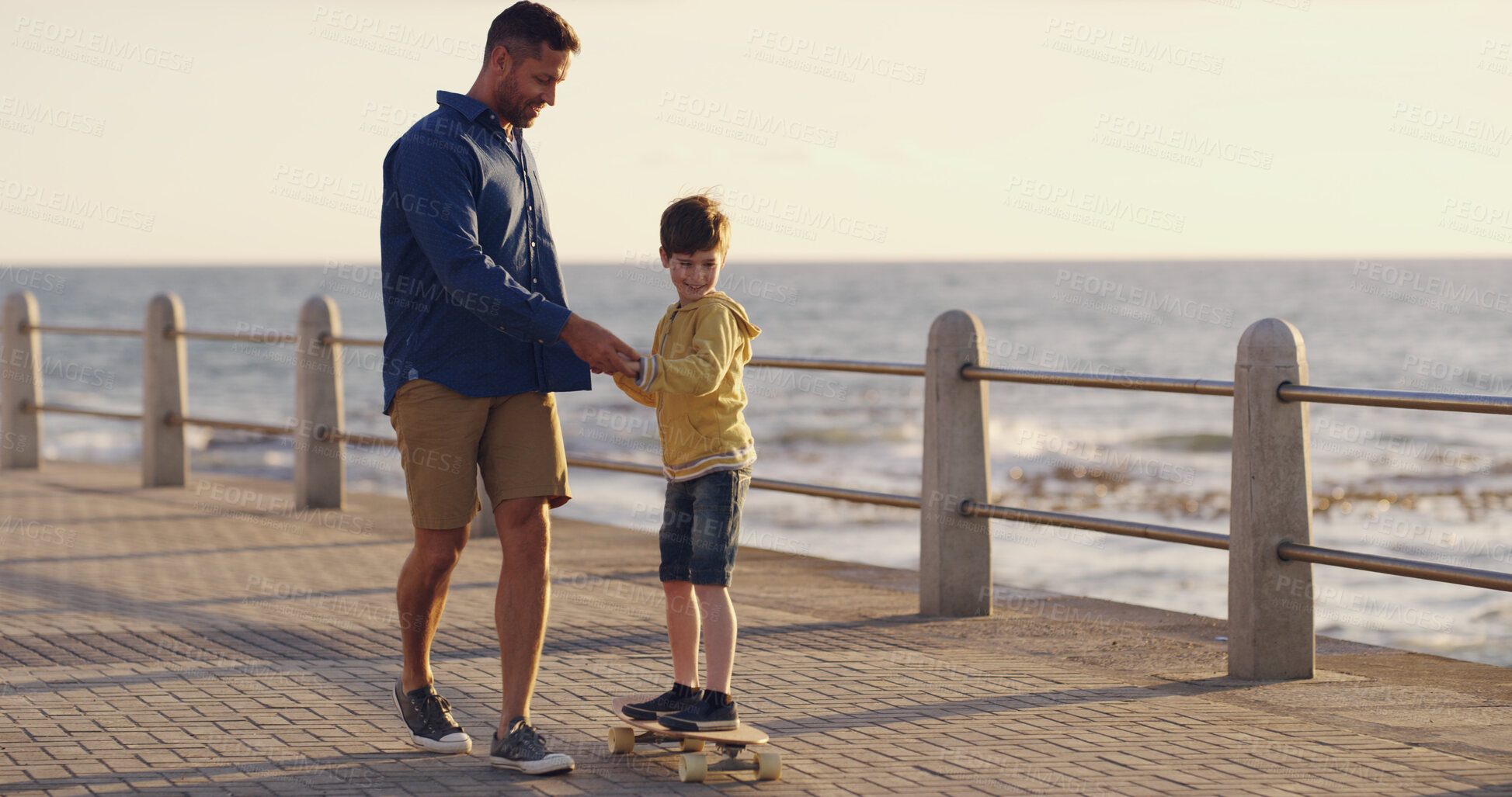 Buy stock photo Dad, son and outdoor for learning skateboard, adventure and sea vacation for bonding with father. Boy, child and papa for support in relationship, helping kid and promenade for love or care on trip