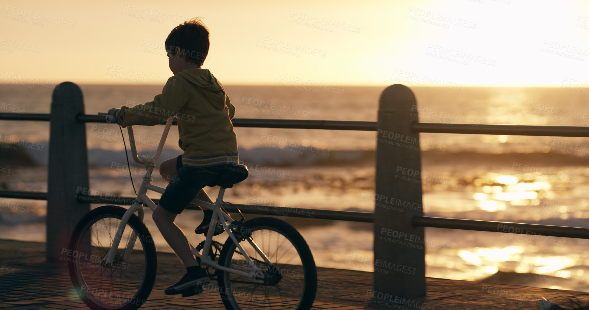 Buy stock photo Boy, kid and bicycle at sunset, beach and promenade with memory, riding and journey on vacation in summer. Child, outdoor and bike with cycling, adventure and playful on pier by ocean in New Zealand