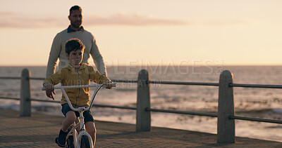 Buy stock photo Dad, boy and bicycle at sunset, beach and promenade with teaching, support and happy on vacation. Father, child and bike with learning, adventure and playful with bonding by ocean in New Zealand