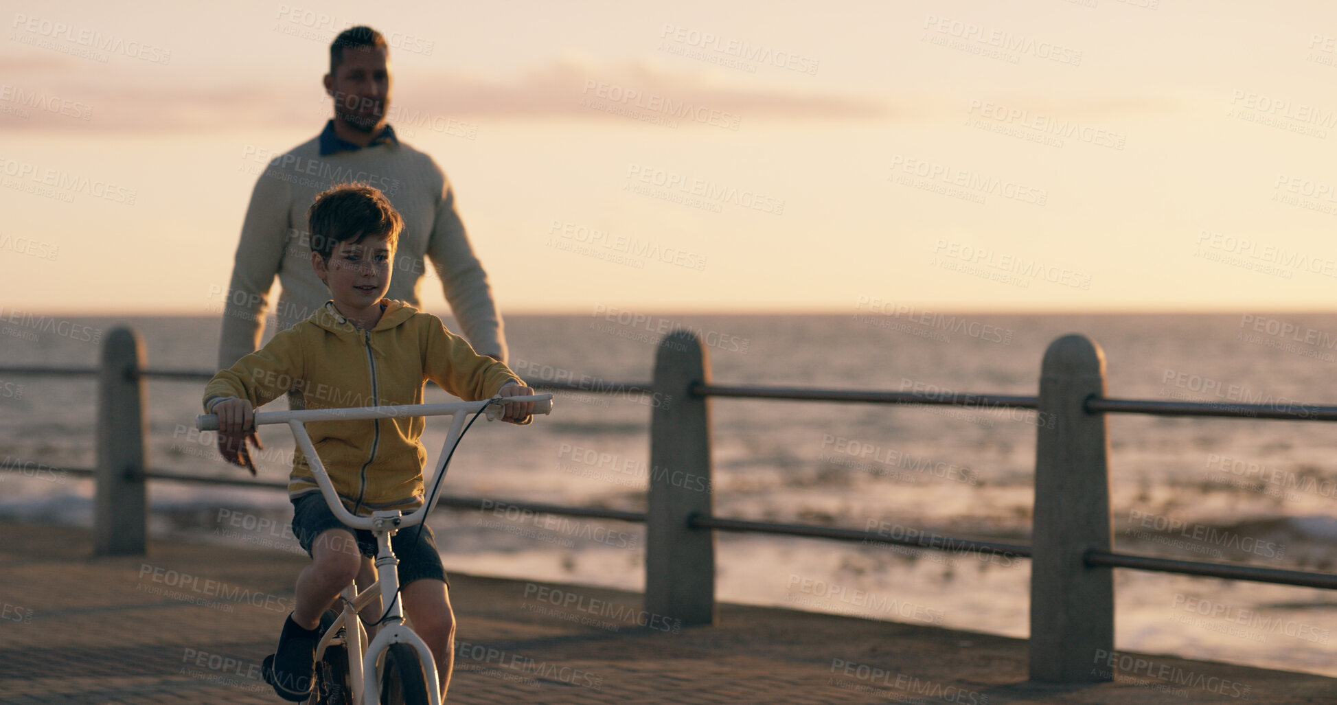 Buy stock photo Dad, boy and bicycle at sunset, beach and promenade with teaching, support and happy on vacation. Father, child and bike with learning, adventure and playful with bonding by ocean in New Zealand