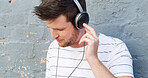 Headphones, relax and man by wall for music or streaming playlist and online radio on gray background. Listening, outdoor and male person in city for learning language on podcast with audio sound