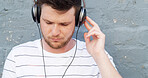 Headphones, outdoor and man by wall for music, streaming zen playlist and radio on gray background. Relax, calm and male person in city for listening to binaural beats on podcast with audio sound