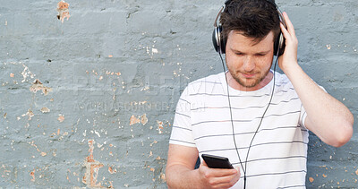 Buy stock photo Man, headphones and phone with music on wall background for audio streaming or sound track. Male person, tourist or casual listener with earphones for playlist, rhythm or podcast in urban town space