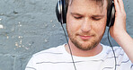 Headphones, listening and man by wall for music or streaming playlist and online radio on gray background. Relax, outdoor and male person in city for learning language on podcast with audio sound