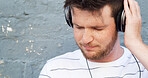 Headphones, relax and man by wall for radio or streaming playlist and music on gray background. Listening, outdoor and calm male person in city for learning language on podcast with zen audio sound
