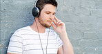 Headphones, calm and man by wall for music, streaming zen playlist and radio on gray background. Relax, outdoor and male person in city for listening to binaural beats on podcast with audio sound