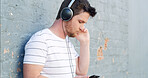 Man, headphones and listening with phone to music on wall background for audio streaming or sound track. Male person, tourist or casual with earphones for playlist, rhythm or podcast in an urban town