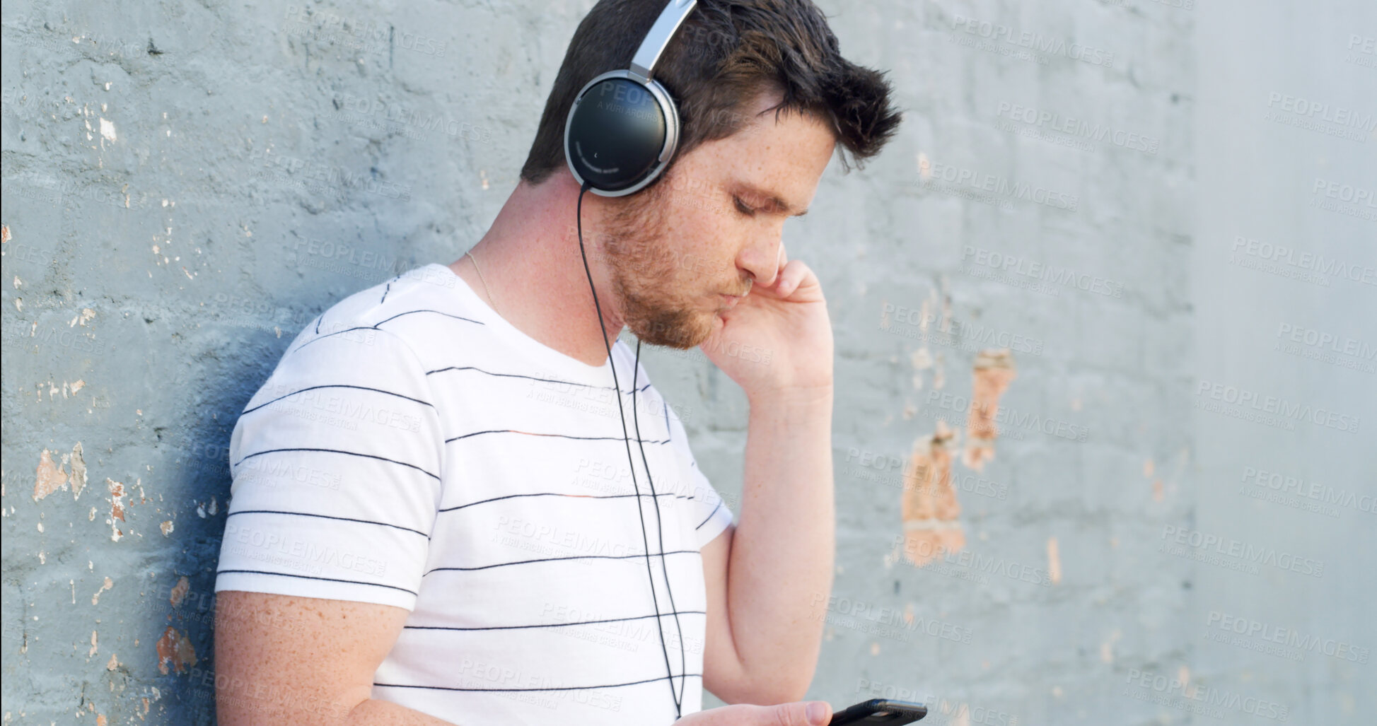 Buy stock photo Man, headphones and listening with phone to music on wall background for audio streaming or sound track. Male person, tourist or casual with earphones for playlist, rhythm or podcast in an urban town