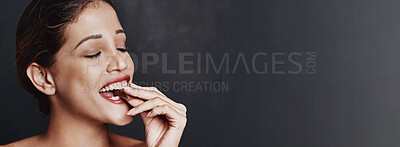 Buy stock photo Happy woman, chocolate and bite with candy in studio for unhealthy diet, sweet or dessert on a dark background. Banner, face or female person with cacao, delight or delicious treat on mockup space