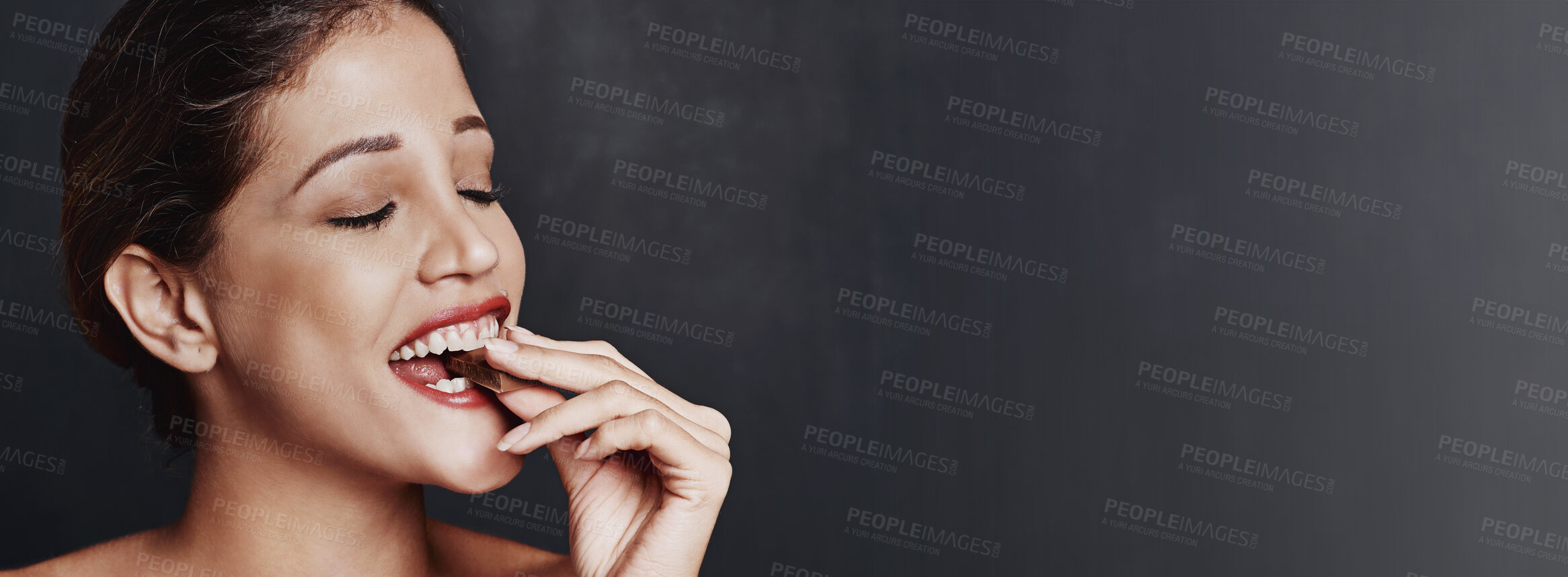 Buy stock photo Happy woman, chocolate and bite with candy in studio for unhealthy diet, sweet or dessert on a dark background. Banner, face or female person with cacao, delight or delicious treat on mockup space