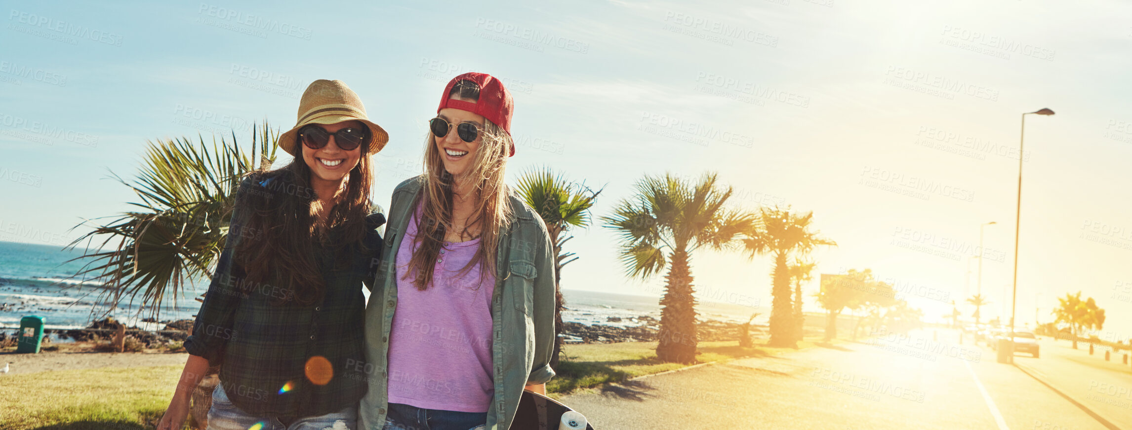 Buy stock photo Walking, friends and women by ocean with skateboard for holiday, banner and vacation trip. Smile, promenade or happy people at beach laughing on break for outdoor activity, bonding and fun adventure