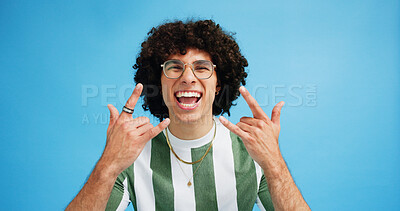Buy stock photo Portrait, rock on and hand gesture with man in studio on blue background with crazy, energy and shout. Rocker, hardcore and male person posing with devil horns, sign or symbol for concert freedom