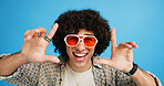 Happy man, portrait or sunglasses with hairstyle or funky fashion on a blue studio background. Male person, hipster or young model with stylish shades or finger frame for summer party or festive mood