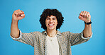 Happy man, portrait and winning with fist pump for celebration or promotion on a blue studio background. Excited, male person or young model with smile in joy for victory, prize or holiday deal