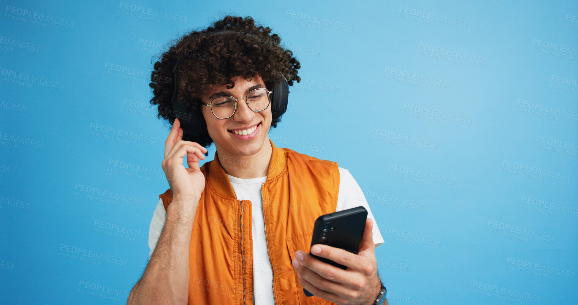 Buy stock photo Happy man, phone and listening with headphones in studio for music or audio streaming on a blue background. Male person, model or user with smile on mobile smartphone for sound playlist on space