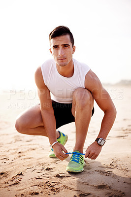 Buy stock photo Man, fitness and tie shoe on beach with thinking, start and ready for run at seaside. Runner, serious and tying sneakers at ocean for wellness, sports and outdoor with training commitment in Portugal