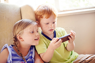 Buy stock photo Curious, siblings and children with smartphone, watching and smile for movies in home, sofa or online. House, fun and kids with mobile for entertainment, streaming or subscription for film in lounge