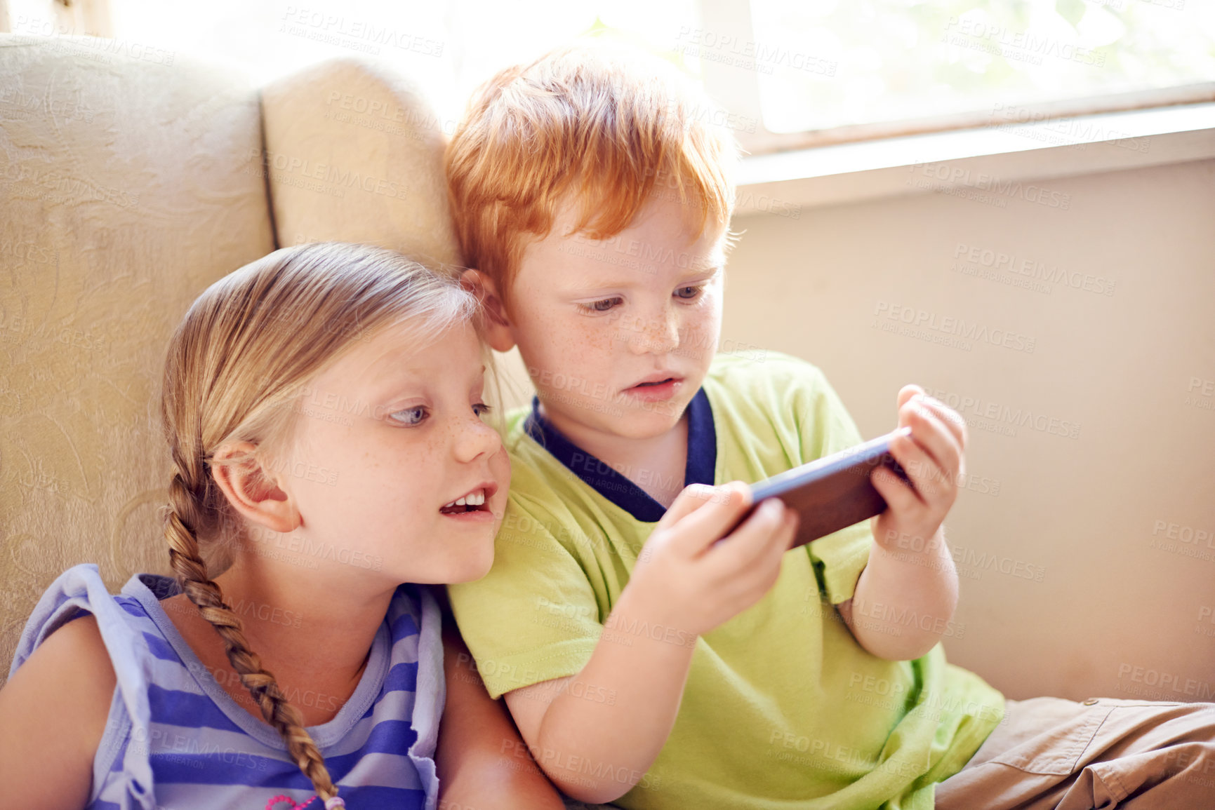 Buy stock photo Curious, siblings and children with smartphone, watching and smile for movies in home, sofa or online. House, fun and kids with mobile for entertainment, streaming or subscription for film in lounge