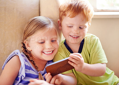 Buy stock photo Fun, siblings and children with smartphone, watching and smile for movies in home, sofa or online. House, relax and kids with mobile for entertainment, streaming or subscription for film in lounge