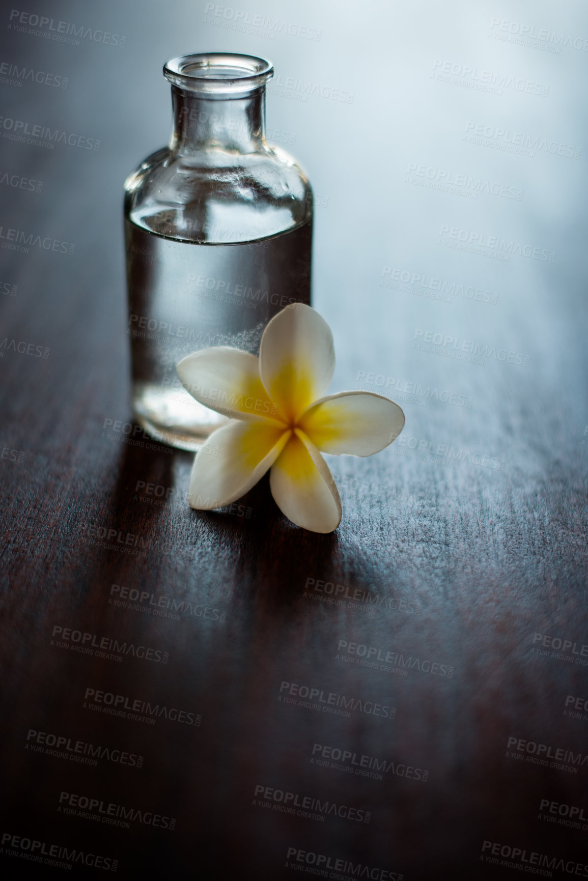 Buy stock photo Body care, luxury and essential oil with flower on table for skin moisturizer, stress relief or aromatherapy massage. Interior space, cosmetics and natural extract for skincare, antioxidants or relax
