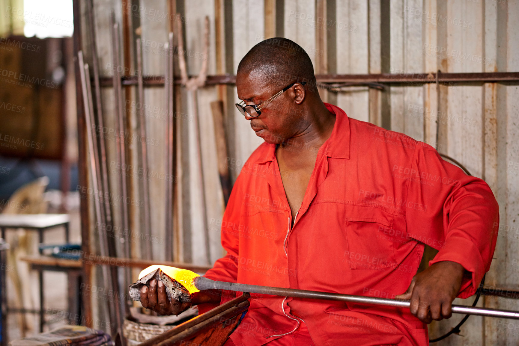 Buy stock photo Glass blowing, glow and black man in workshop for creative small business, artist and handmade process. Art, product shape and glassblower in factory for sustainable project, design or craft tools