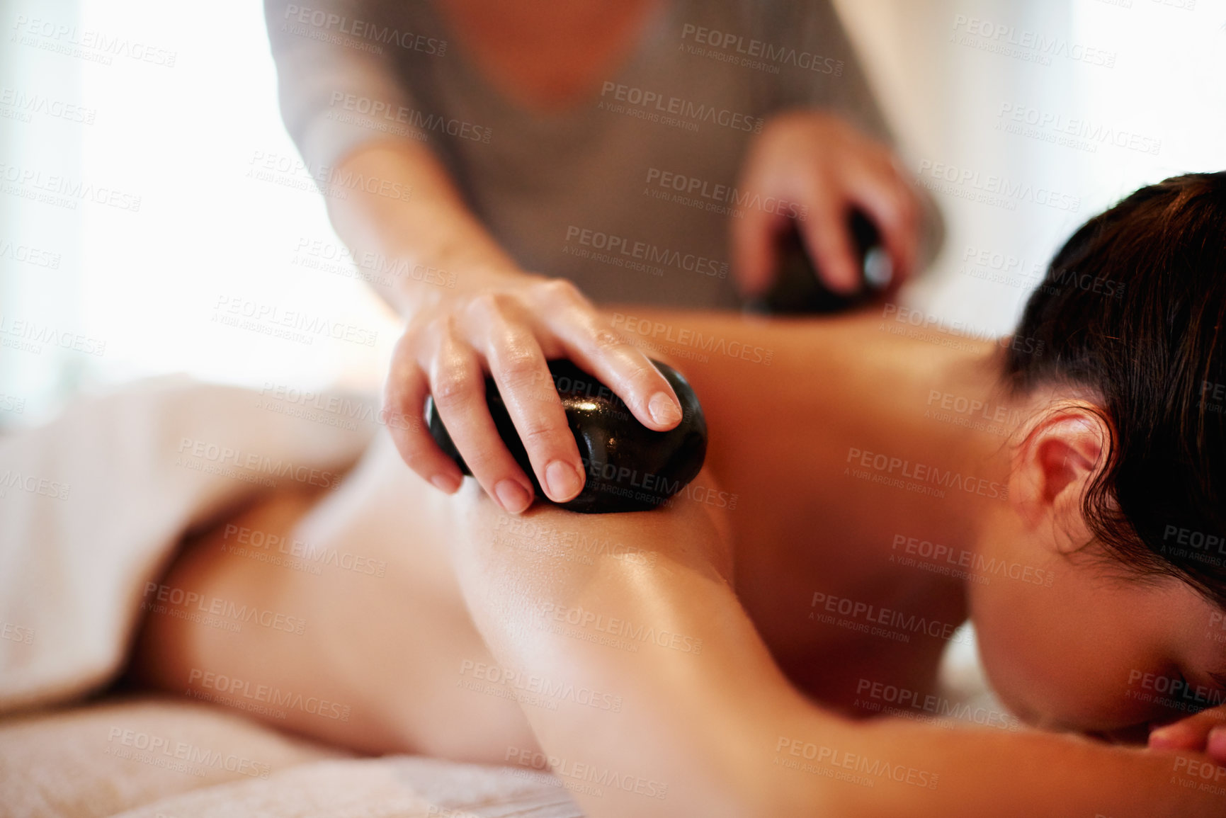 Buy stock photo Hot stone, massage and woman on bed at spa with hospitality, peace and healthy self care at luxury hotel service. Relax, therapist and girl on table at wellness clinic for holistic muscle treatment.