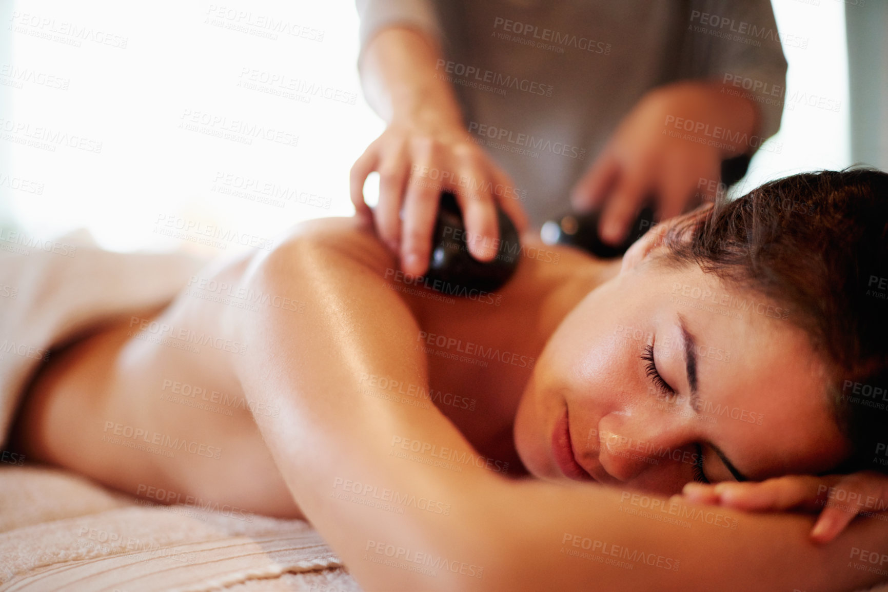 Buy stock photo Stone, massage and woman on table at spa with hospitality, peace and healthy self care at luxury hotel service. Relax, therapist and girl on bed at wellness clinic for holistic back muscle treatment.