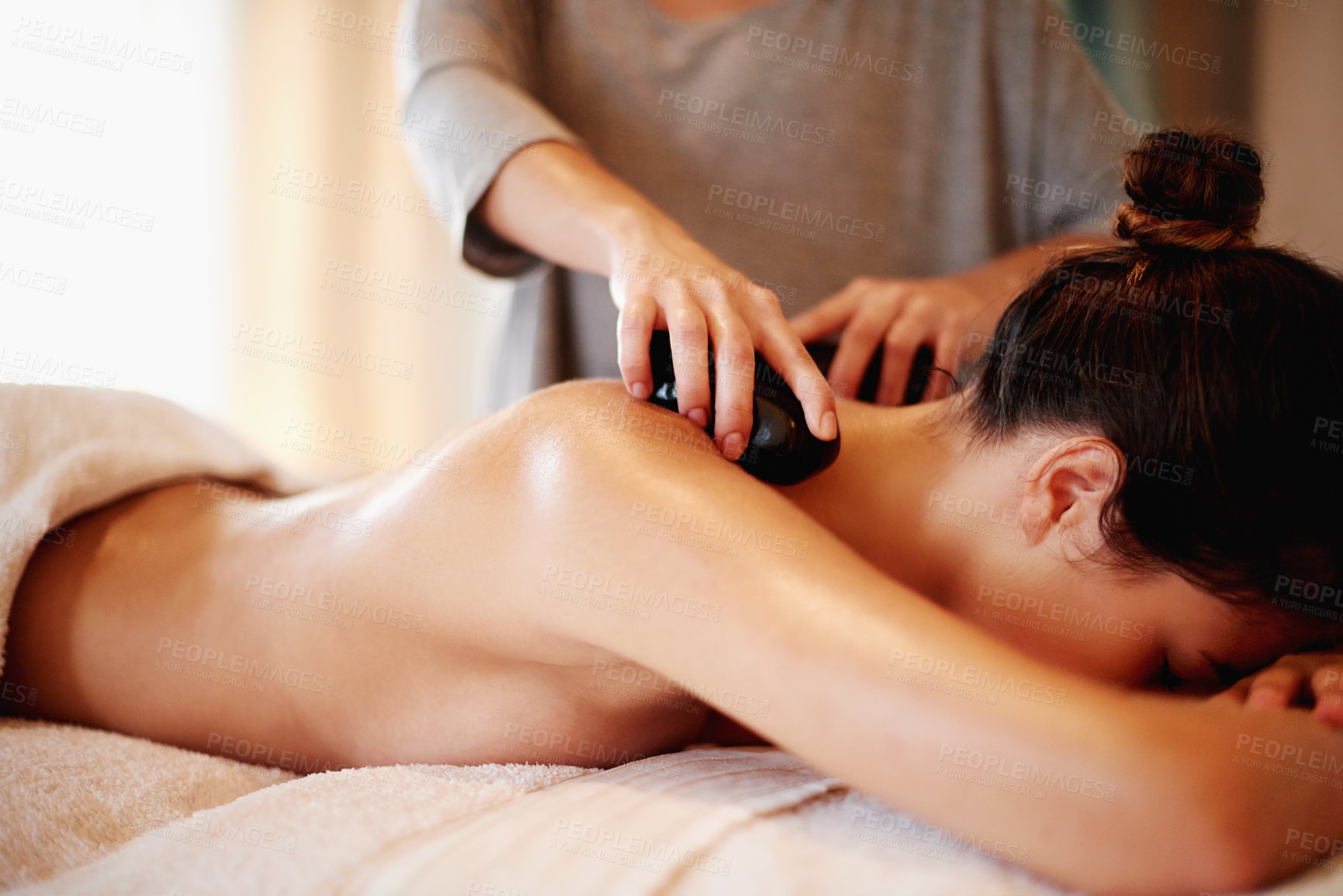 Buy stock photo Stone, massage and woman on bed at spa with hospitality, peace and healthy self care at luxury hotel service. Relax, therapist and girl on table at wellness clinic for holistic back muscle treatment.