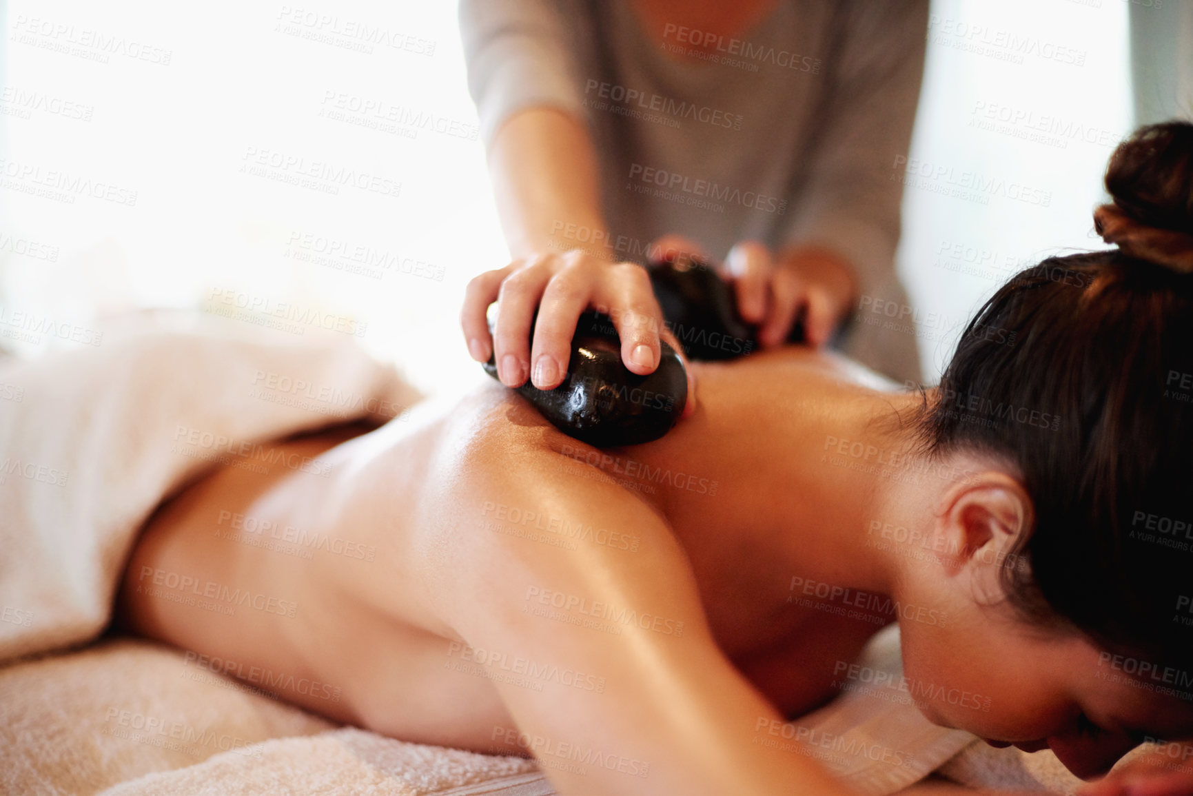 Buy stock photo Hands, resort and hot stone massage for back, muscle recovery and stress relief on holiday at spa. Woman, masseuse and service with rock for circulation, relax and healing tissue at luxury lodge