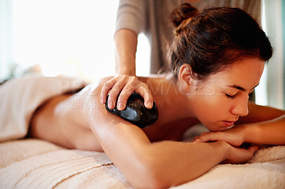 Buy stock photo Girl, spa and hot stone massage for back pain, muscle recovery and stress relief on holiday at lodge. Woman, masseuse and service with rock for circulation, relax and healing tissue at luxury resort
