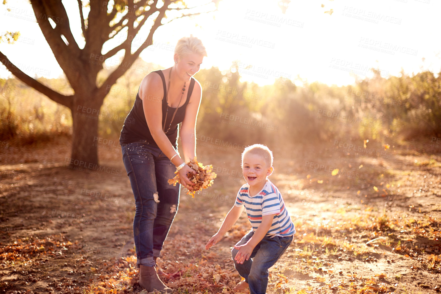 Buy stock photo A mother and son being playful and throwing leaves into the air at the park