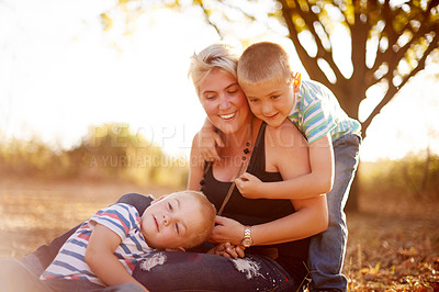 Buy stock photo Children, mother and hug on grass with love, support or relax at sunset on summer vacation. Happy woman, kids or playful in nature for family holiday, bonding or relationship development for wellness