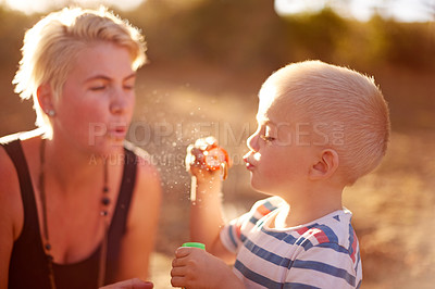 Buy stock photo Happy, blowing bubbles and child in park with mom for fun, childhood and bonding together outdoors. Family, sunlight and woman with young boy with soap wand, toys and activity for playing in nature