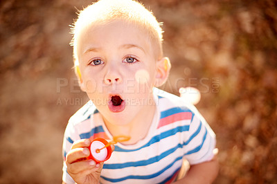 Buy stock photo Shot of a cute little boy blowing bubbles in the outdoors