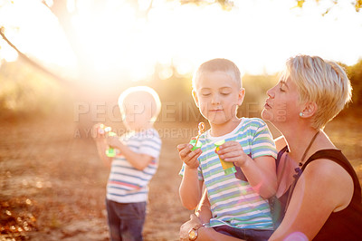 Buy stock photo Happy, blowing bubbles and children in nature with mom for fun, childhood and bonding together outdoors. Family, sunlight and mother with kids with soap, toys and activity for playing games in park
