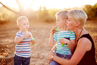 Buy stock photo Happy, blowing bubbles and children in park with mom for fun, childhood and bonding together outdoors. Family, sunlight and mother with boys with soap wand, toys and activity for playing in nature
