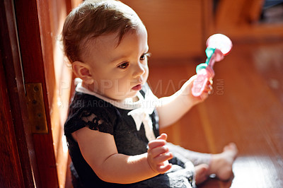 Buy stock photo Baby, rattle and toy in home for relax, sensory development and child growth. Girl toddler, plastic shaker and playing in living room for wellness, learning and fidget with teething ring on floor