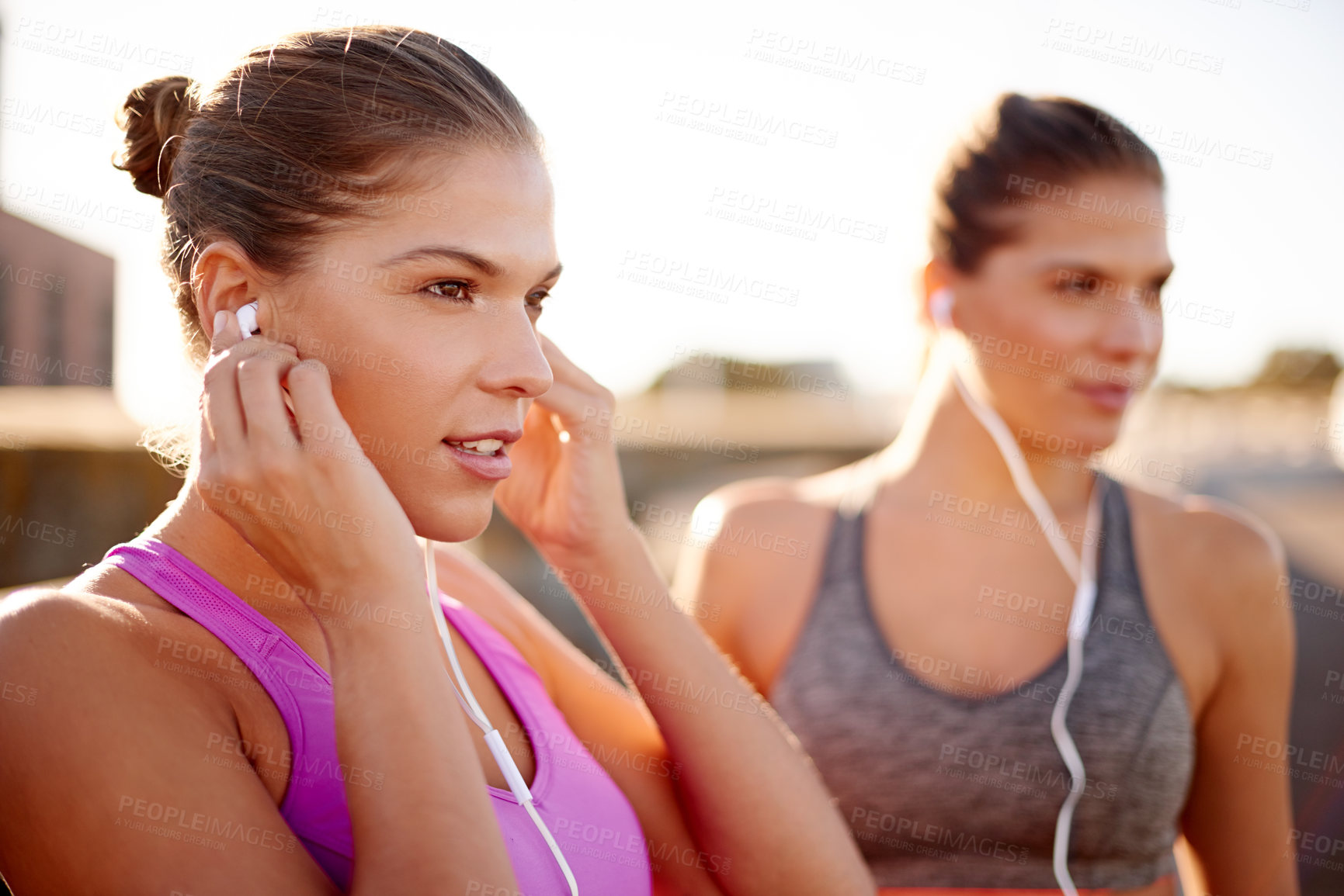 Buy stock photo Women, fitness and together with earphones in street for music, training and sisters in summer. People, runner and twins with streaming, subscription and happy for workout on urban bridge in Spain