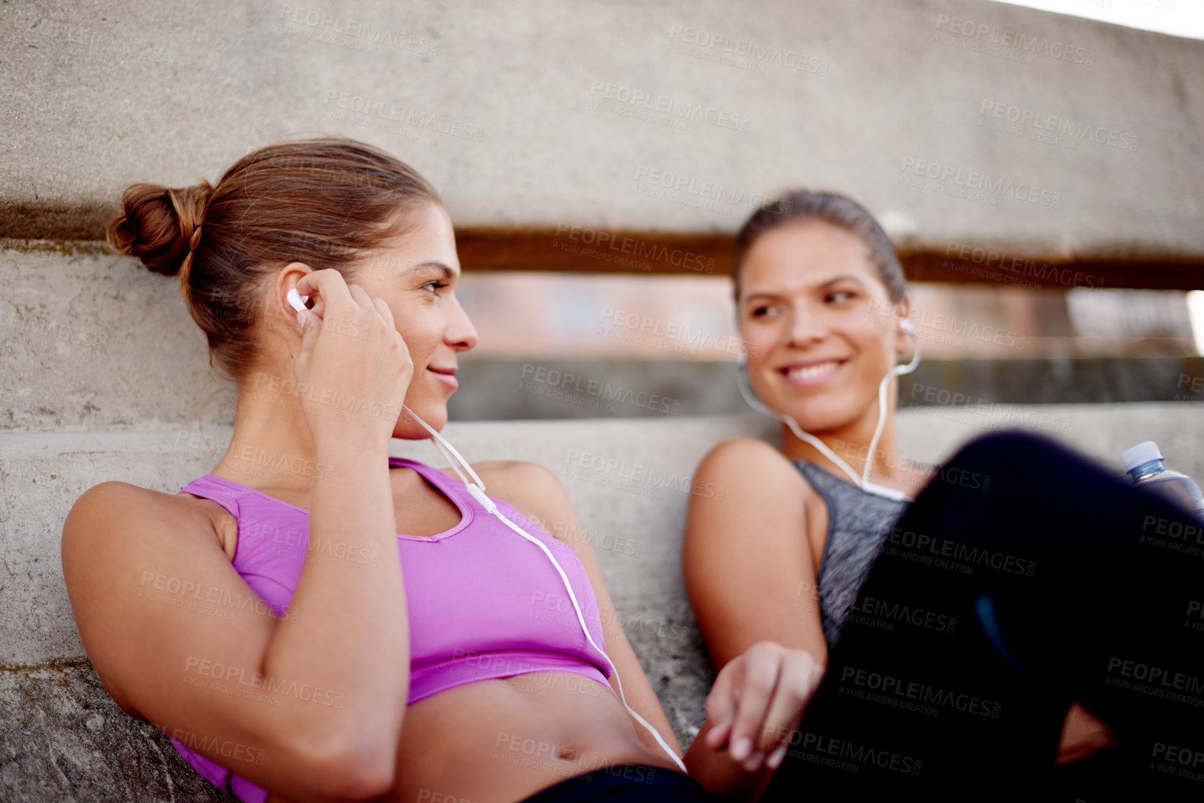 Buy stock photo Fitness, women and break with music outdoor for cardio challenge, listening to sound track and recovery. Twin teamwork, happy and relax on bridge with earphones for workout audio and training support