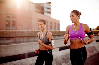 Buy stock photo Women, running and together in road with earphones, training and prepare for marathon in city. People, twins and sisters with exercise, streaming or cardio workout on bridge with smile in Australia