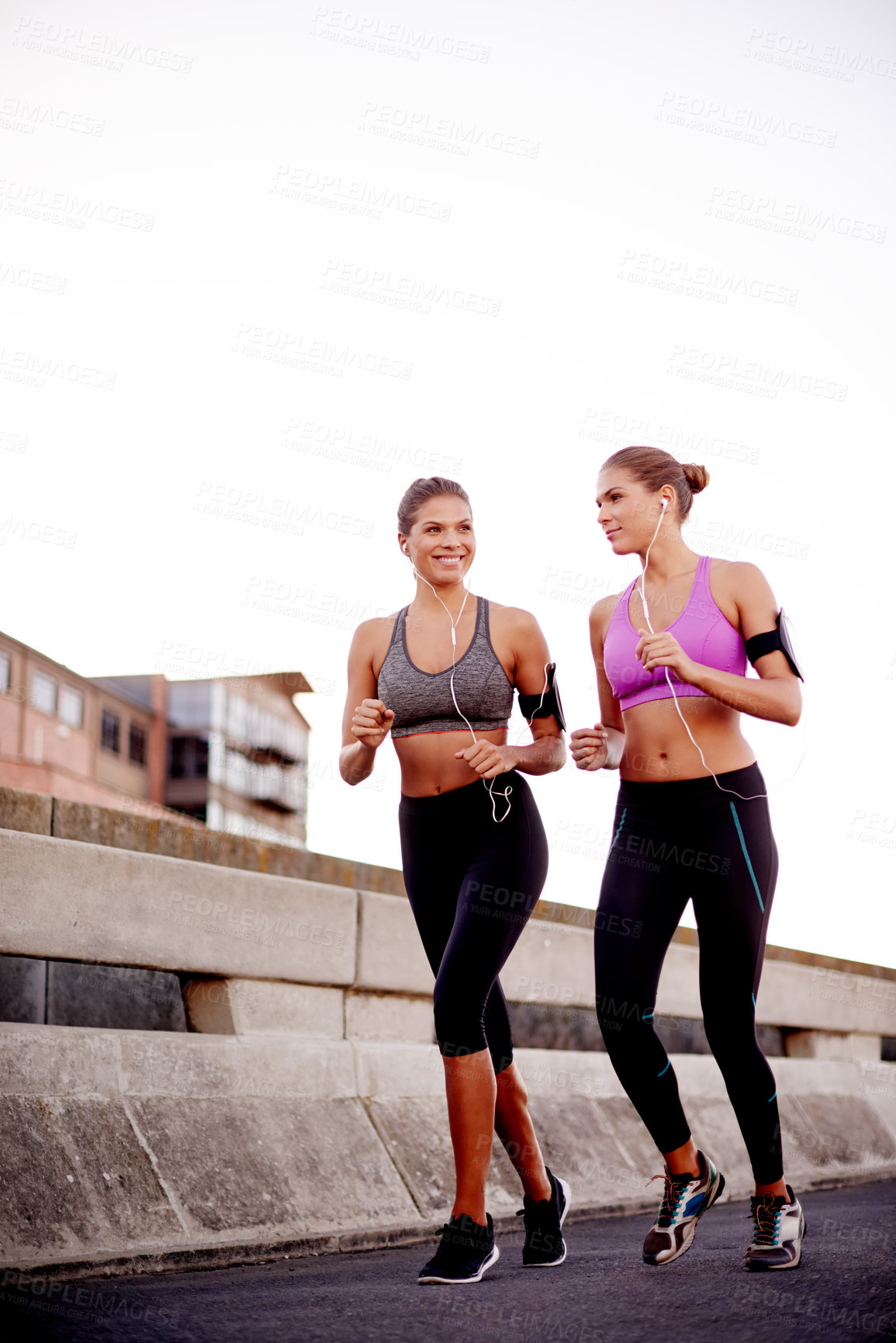 Buy stock photo Women, running and team in road with earphones, training and wearable tech on urban bridge. People, twins and sisters with exercise, streaming or smile for cardio workout with mockup space in Germany