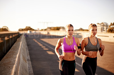 Buy stock photo Women, workout and bridge for running in city, streaming sound and team support with exercise. Urban town, fitness together and podcast for cardio sports, marathon training and earphones for twins
